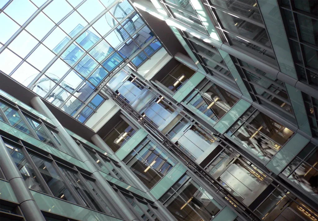 Upward view of a modern office building's central atrium with a transparent ceiling and geometric metal structure.