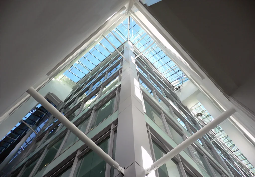 Upward view of a modern office building's central atrium with a transparent ceiling and geometric metal structure.