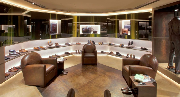 Curved boutique interior showcasing a variety of shoes on lit shelves, leather chairs, and patina glass walls.