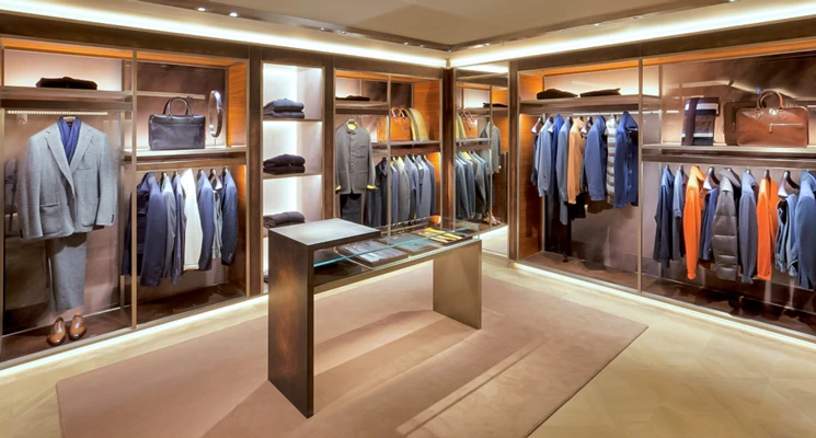 Upscale men's clothing boutique interior with lit wooden cabinets showcasing suits and accessories.