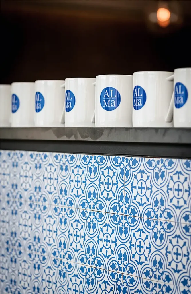 Row of white mugs with blue logos atop a service station featuring traditional Portuguese blue and white ceramic tiles.