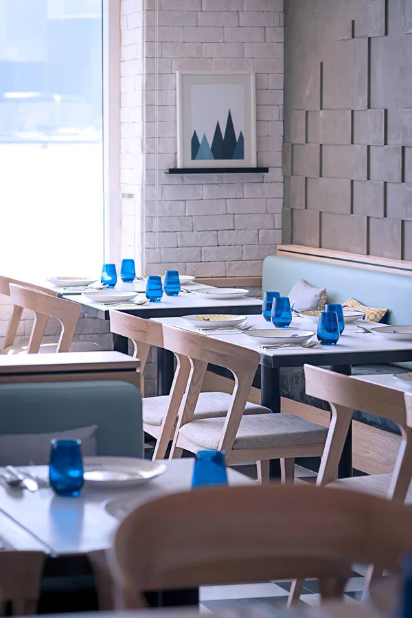 Modern dining area with blue glassware on wooden tables, light brick walls, and abstract art.