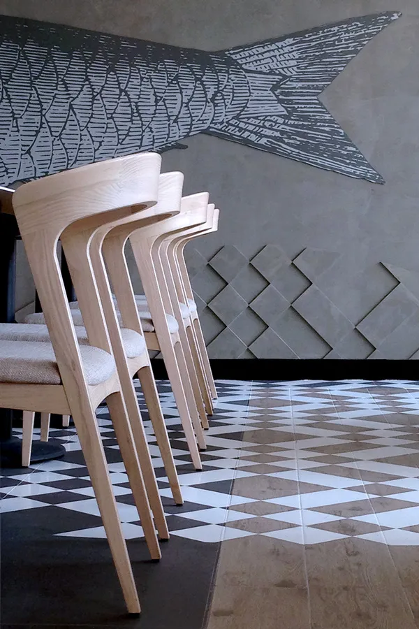 Stacked wooden chairs with a fish mural and geometric floor in a restaurant.