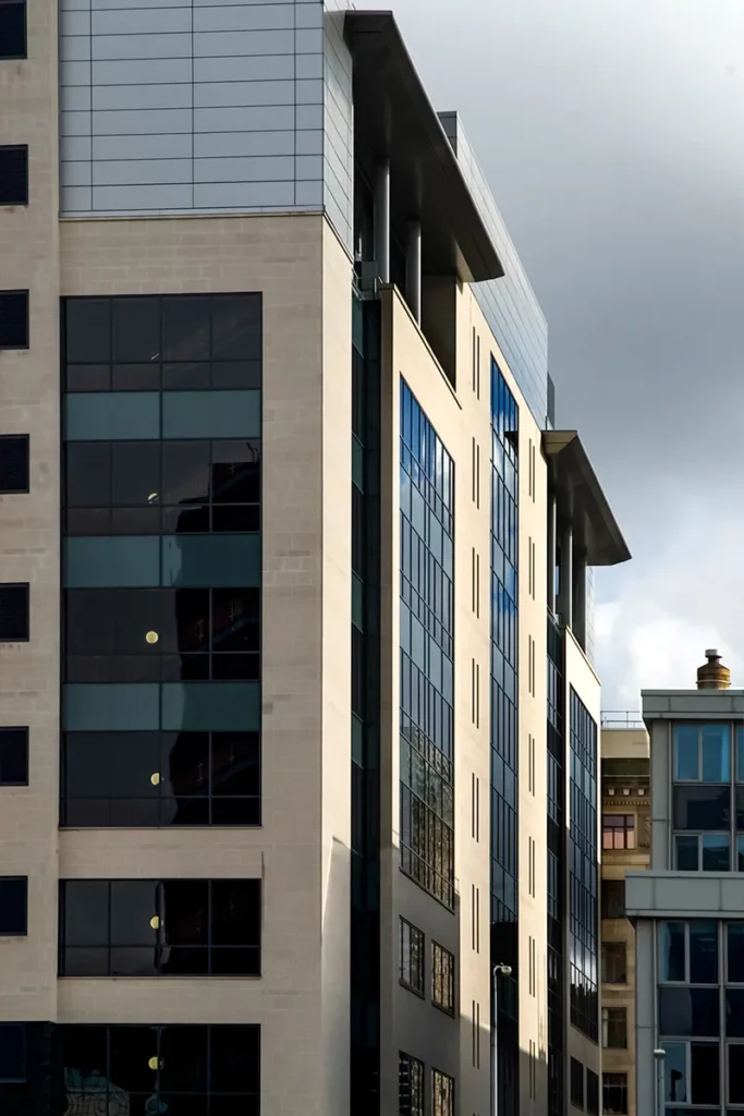 Side view of a contemporary office building featuring a combination of glass windows and stone facade, highlighted by contrasting geometric lines and a metallic zinc roof.